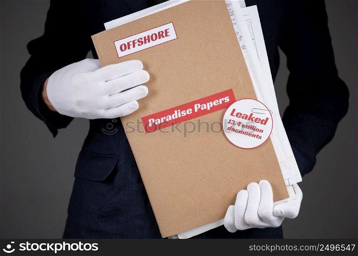 Man in suit and white gloves hold paper folder with Paradise Papers and Offshore label with documents inside, tax heaven documents leak concept