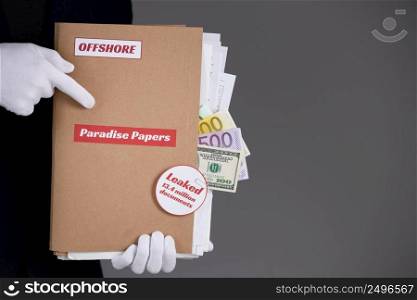 Man in suit and white gloves hold paper folder with Paradise Papers and Offshore label with documents and money inside, tax heaven documents leak concept