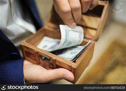 Man in suit holding tray full of money. Groom holding dollars in casket