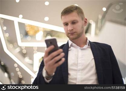 man in suit indoors looks at smartphone