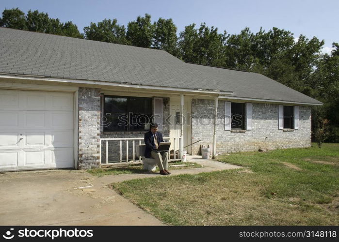 Man in suit with laptop sitting on toliet outside home.