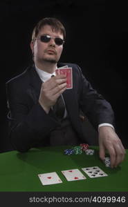 Man in suit with sun glasses playing poker on green table. Chips and cards on the table.