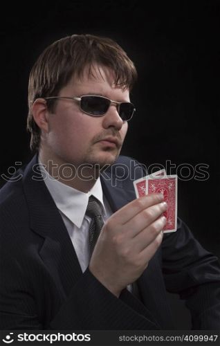 Man in suit with sun glasses playing poker on green table. Chips and cards on the table.