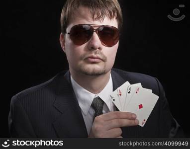 Man in suit with sun glasses playing poker on green table. Chips and cards on the table.