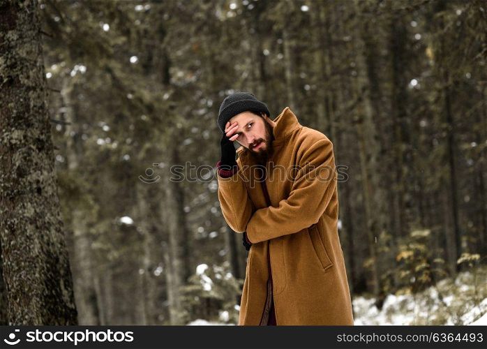 man in the winter forest is cold and in a brown coat and gloves
