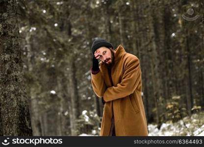 man in the winter forest is cold and in a brown coat and gloves