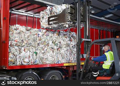 Man in vehicle loading stacks of recycled paper on to lorry