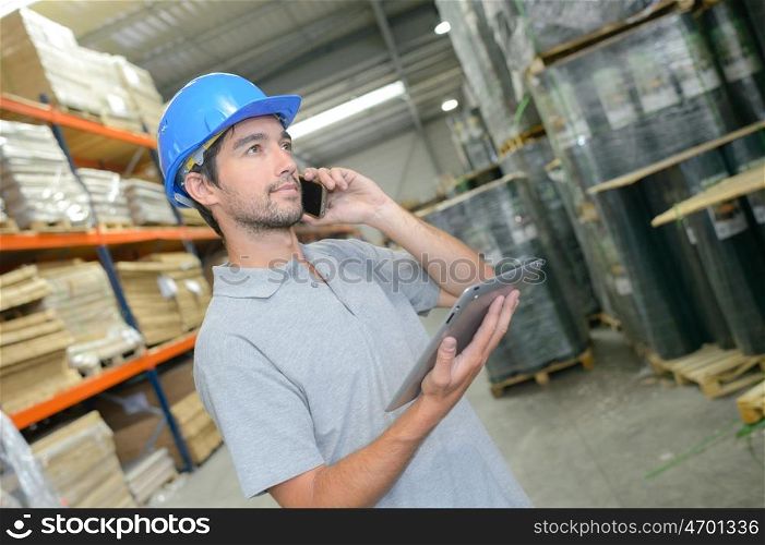 Man in warehouse holding tablet and talking on telephone
