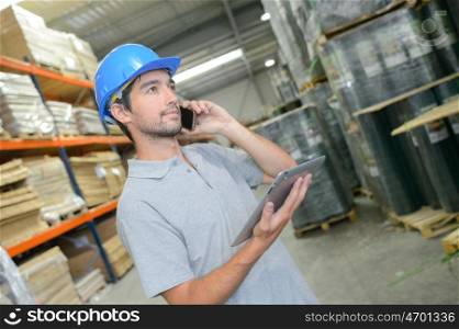 Man in warehouse holding tablet and talking on telephone