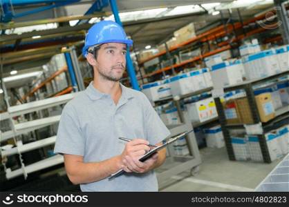 Man in warehouse writing on clipboard