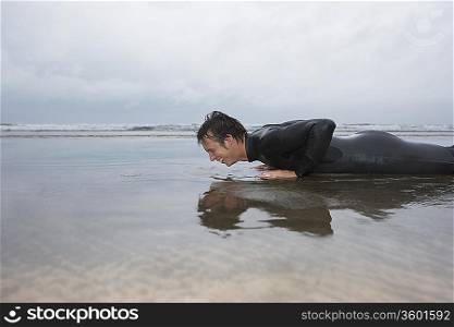 Man in wetsuit doing pushups in shallow water on beach, side view