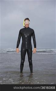 Man in wetsuit wearing snorkle, standing in water on beach, portrait