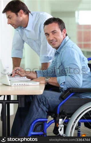 Man in wheelchair at desk working next to colleague