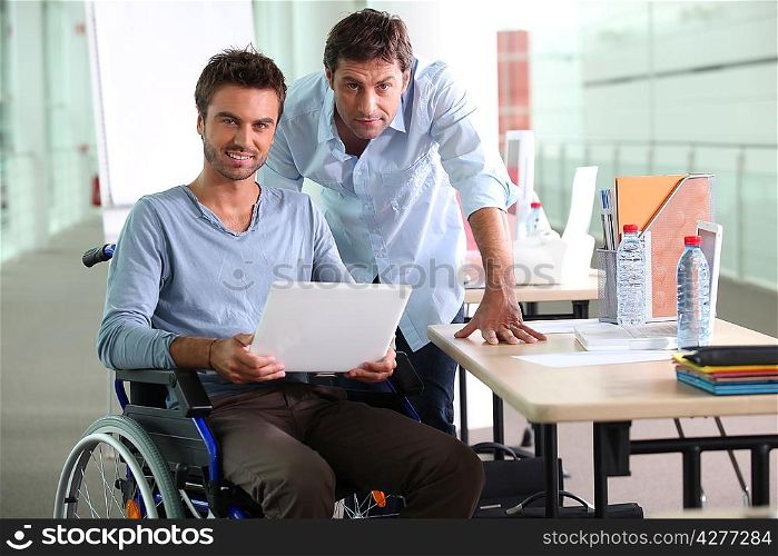 Man in wheelchair holding laptop computer next to colleague
