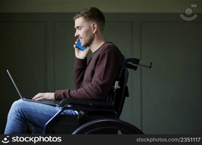 Man in Wheelchair Working From Home Using Laptop And Mobile Phone