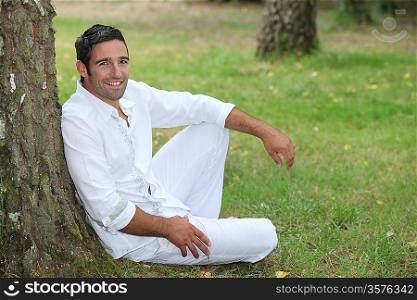 Man in white sitting by a tree
