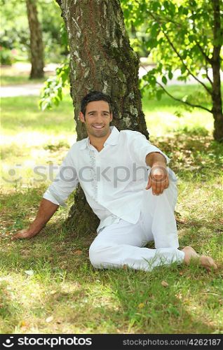 Man in white sitting under a tree