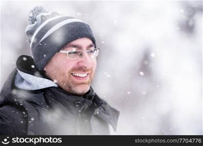 Man in winter season  Portrait of young man in warm clothes enjoying snowy day with snowflakes around him in the winter forest