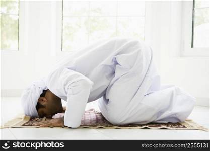Man indoors praying on mat (high key)
