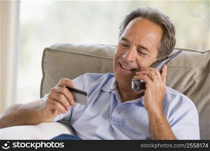 Man indoors using telephone and looking at credit card smiling