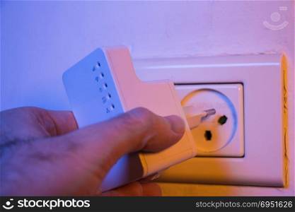 Man insert WiFi repeater into electrical socket on the wall. The device help to extend wireless network in home or office.