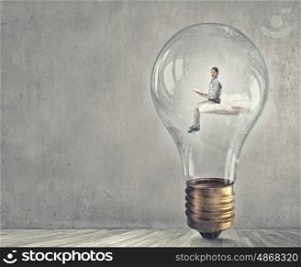 Man inside bulb. Young businessman inside of light bulb reading book