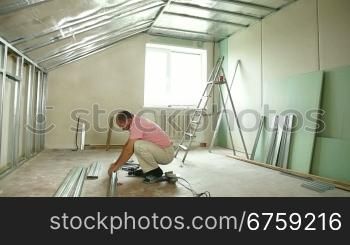 Man installing plasterboard walls in the house, working with screw gun