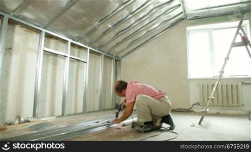 Man installing plasterboard walls in the house, working with screw gun