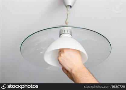man installs lampshade of ceiling lamp at home