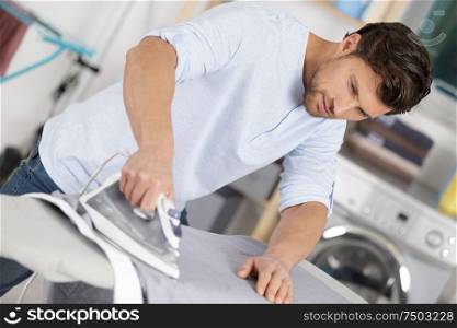 man ironing shirt on iron board at home