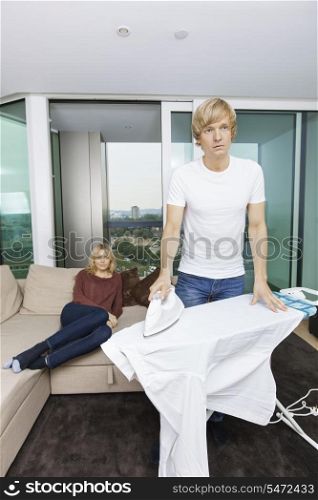 Man ironing shirt while woman sitting on sofa at home