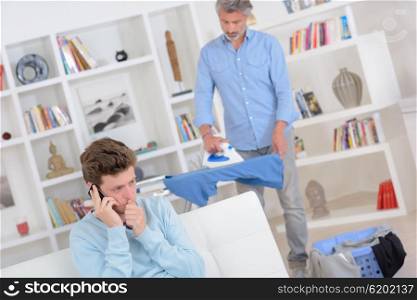 Man ironing, son on telephone