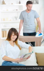 man ironing while wife reading the news on the sofa