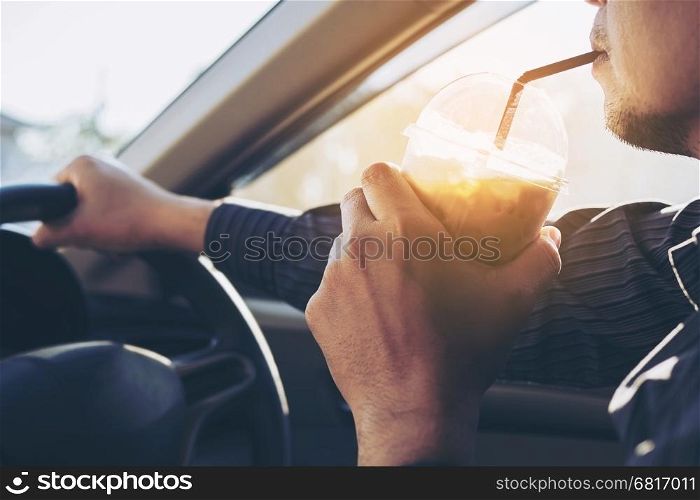 Man is dangerously drinking cup of cold coffee while driving a car