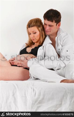 man is embracing his pregnant wife in bed at morning