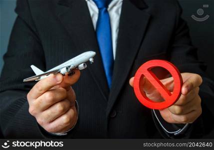 Man is holding an airplane and a red NO sign. Ban on flights. Non-flying zone. Lack of air transporting capacity. Embargo, sanctions. Transport crisis, unprofitable flight routes. Flight cancellation