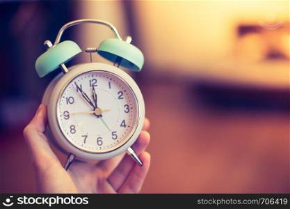 Man is holding an alarm clock, sunshine in the morning, blurry background