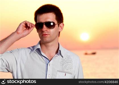 man is holding sunglasses at sunrise near sea
