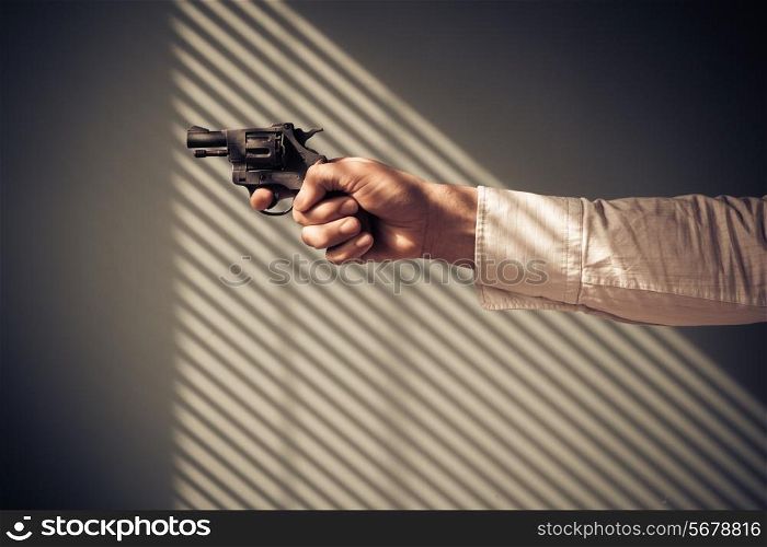 Man is pointing a revolver at a window with shaows from the blinds