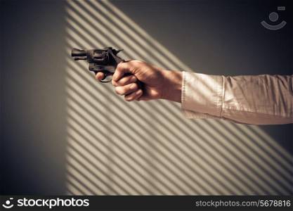 Man is pointing a revolver at a window with shaows from the blinds