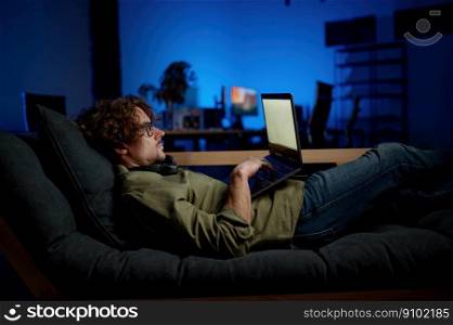 Man IT administrator rest on sofa with laptop computer lying on sofa at modern server room. Night duty in data center concept. Man IT administrator rest on sofa with laptop computer lying on sofa