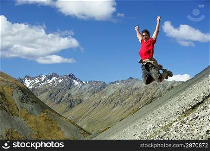 Man jumping down rocky slope with arms raised