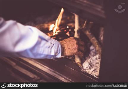 Man kindle a fire in the fireplace, grandpa making warmth and cozy atmosphere in the country house, romantic and peaceful winter evening. Man kindle a fire in the fireplace