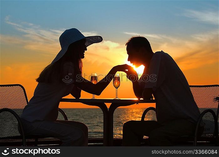 man kisses hand to woman on sunset behind table outside