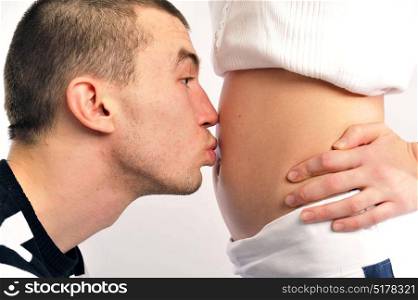 Man kissing his partner on the belly as they expect a baby