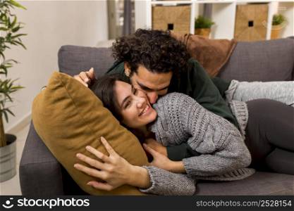 man kissing his smiley wife while lying sofa