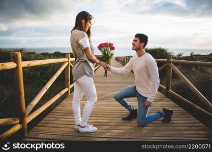 man kneeling handing bouquet roses woman