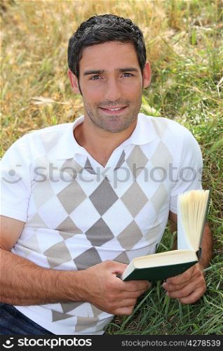 Man laid in field with book in hand