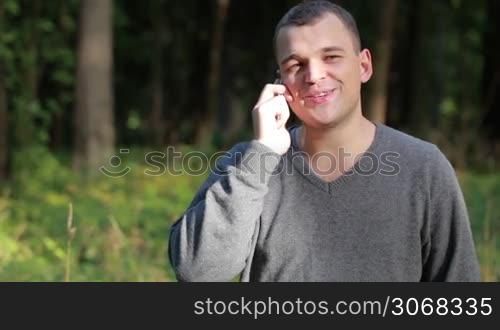 Man laughing as he chats on his mobile phone while standing outdoors in a lush green park with copyspace