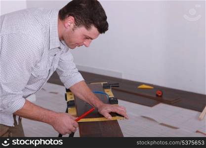 Man laying a floor and measuring a piece of wood